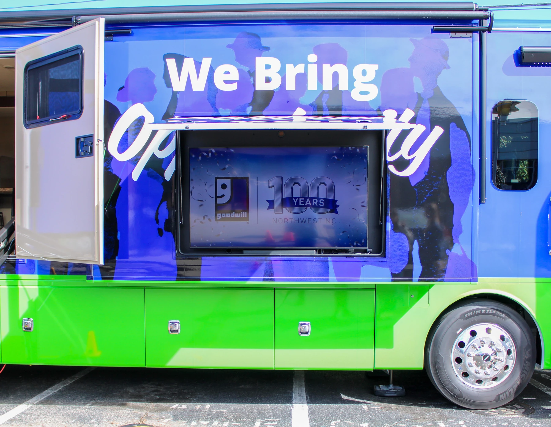 Close view of the installed passenger-side wrap: We Bring Opportunity in white over blue silhouettes, with the exterior screen open and the green lower body below.